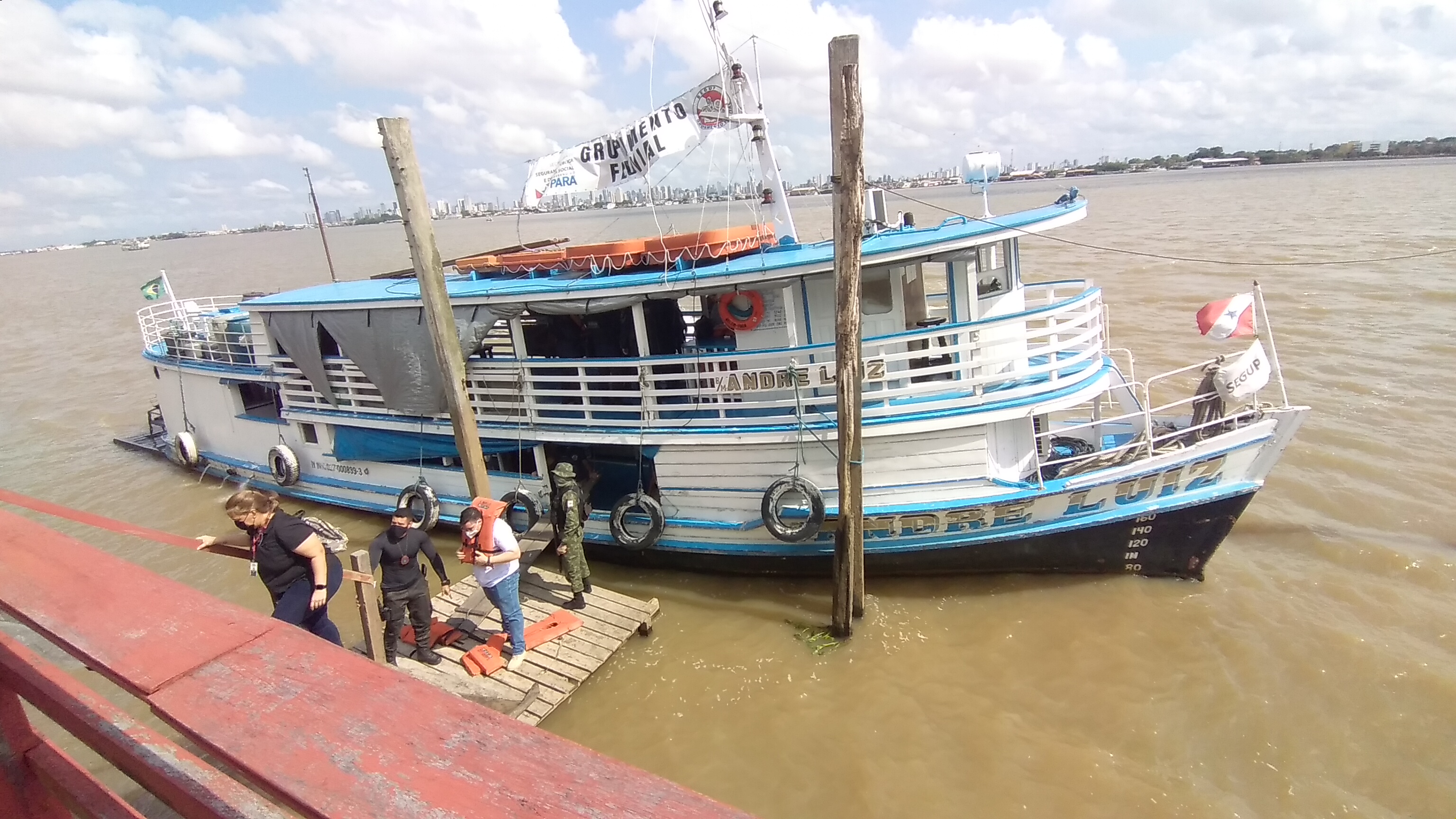 Descrição da imagem: integrantes da ação articulada estão descendo de um dos barcos. Eles caminham em direção a um dos estabelecimentos. O barco é branco e azul celeste, de dois andares. Aparecem o rio e ao fundo a cidade de Belém Descrição da imagem: integrantes da ação articulada estão descendo de um dos barcos. Eles caminham em direção a um dos estabelecimentos. O barco é branco e azul celeste, de dois andares. Aparecem o rio e ao fundo a cidade de Belém
